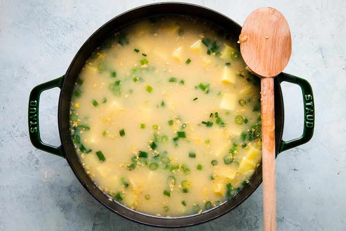 potato and corn chowder ingredients in a stock pot stirred together with a wooden spoon resting on the pot
