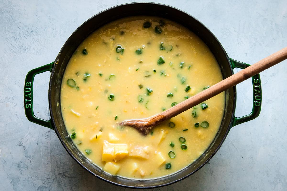 potato and corn chowder in a stock pot with a wooden spoon