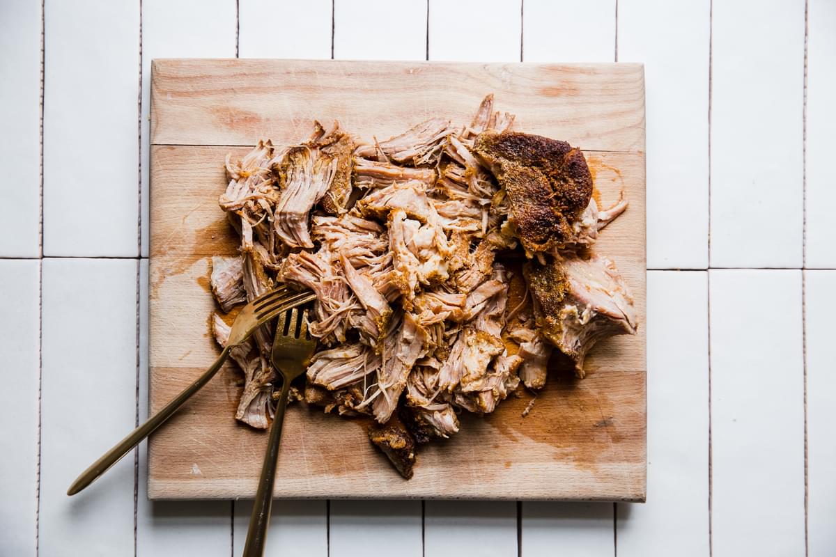 pork shoulder made with spices, chicken stock, and vinegar. shredded on a cutting board with two forks.