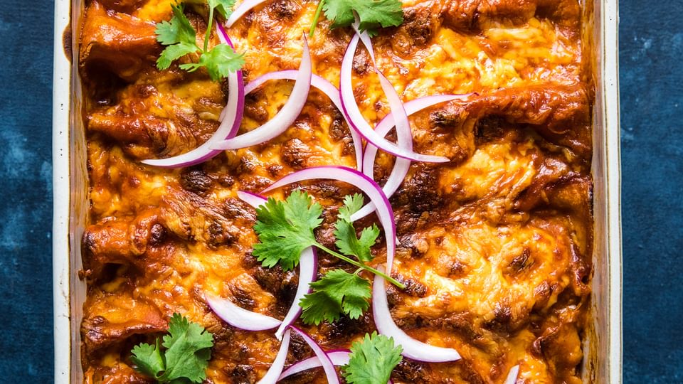 homemade red chicken enchiladas topped with cilantro and red onion