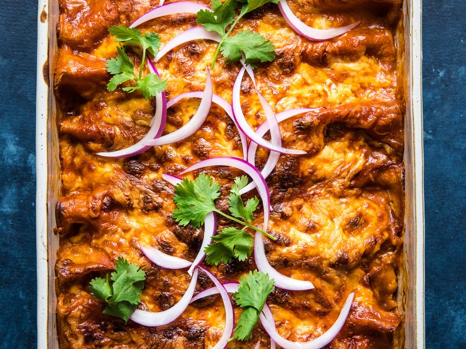 homemade red chicken enchiladas topped with cilantro and red onion