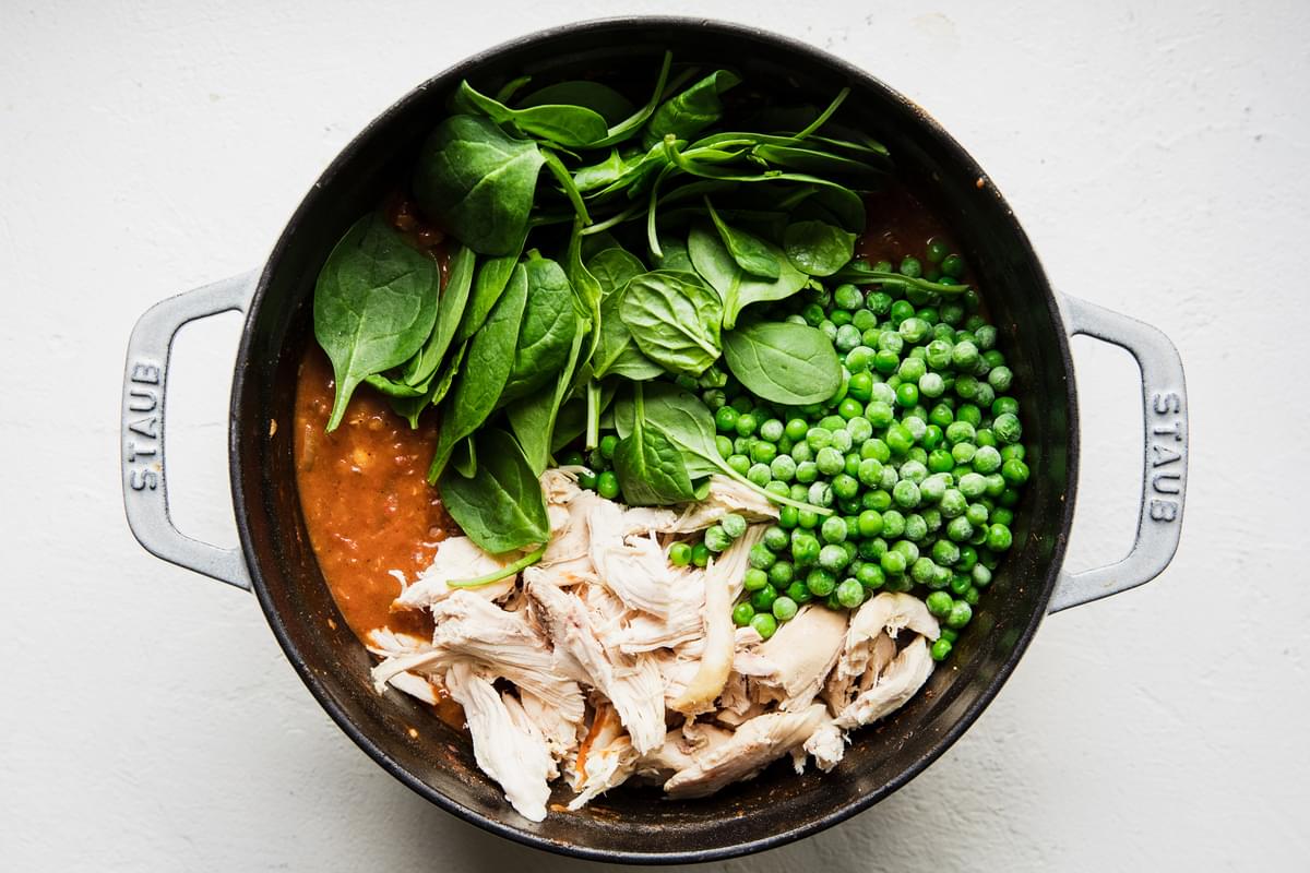 spinach, chicken and peas being added to a pot of red lentil soup