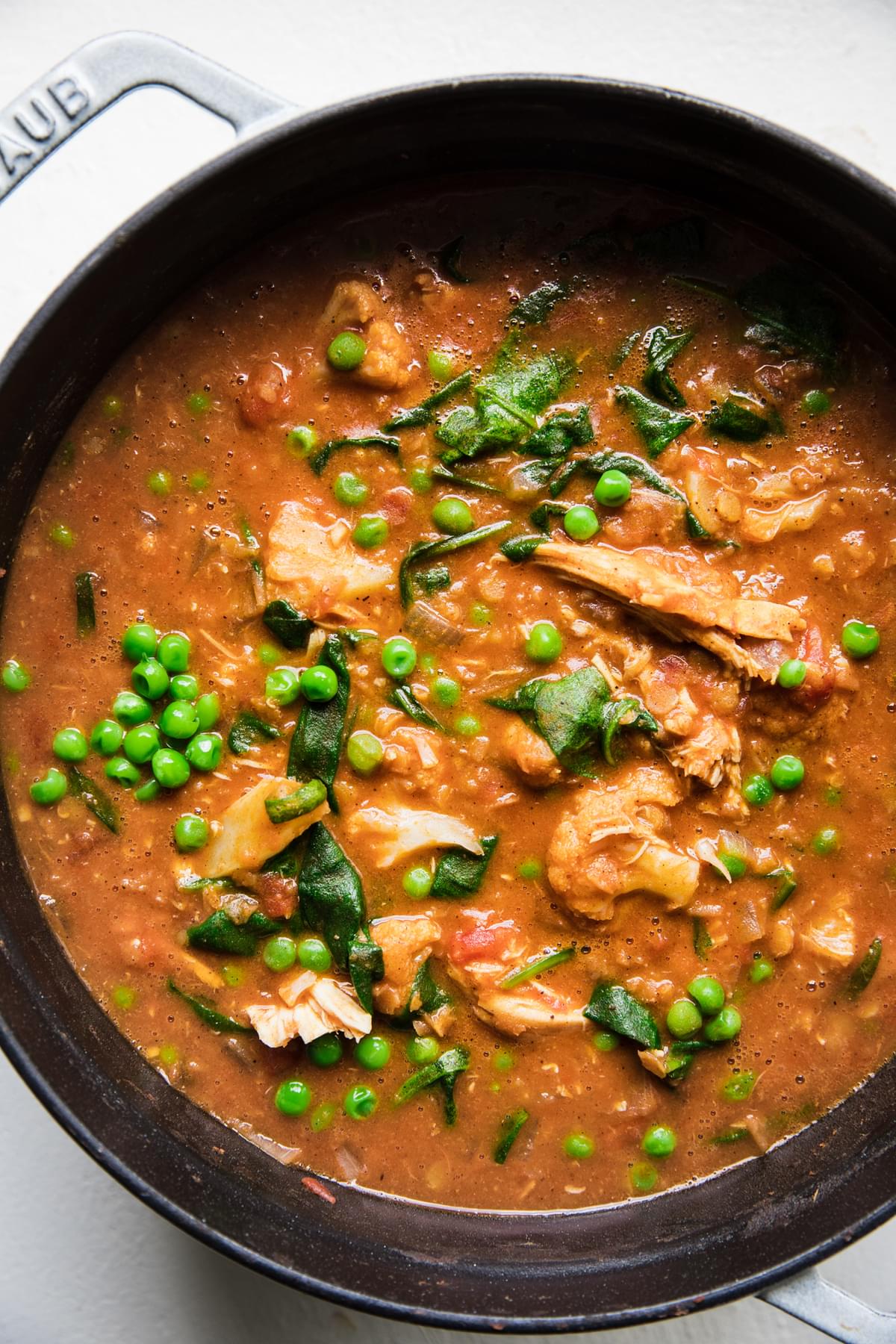 a pot of red lentil soup made with coconut milk, chicken, spinach and peas