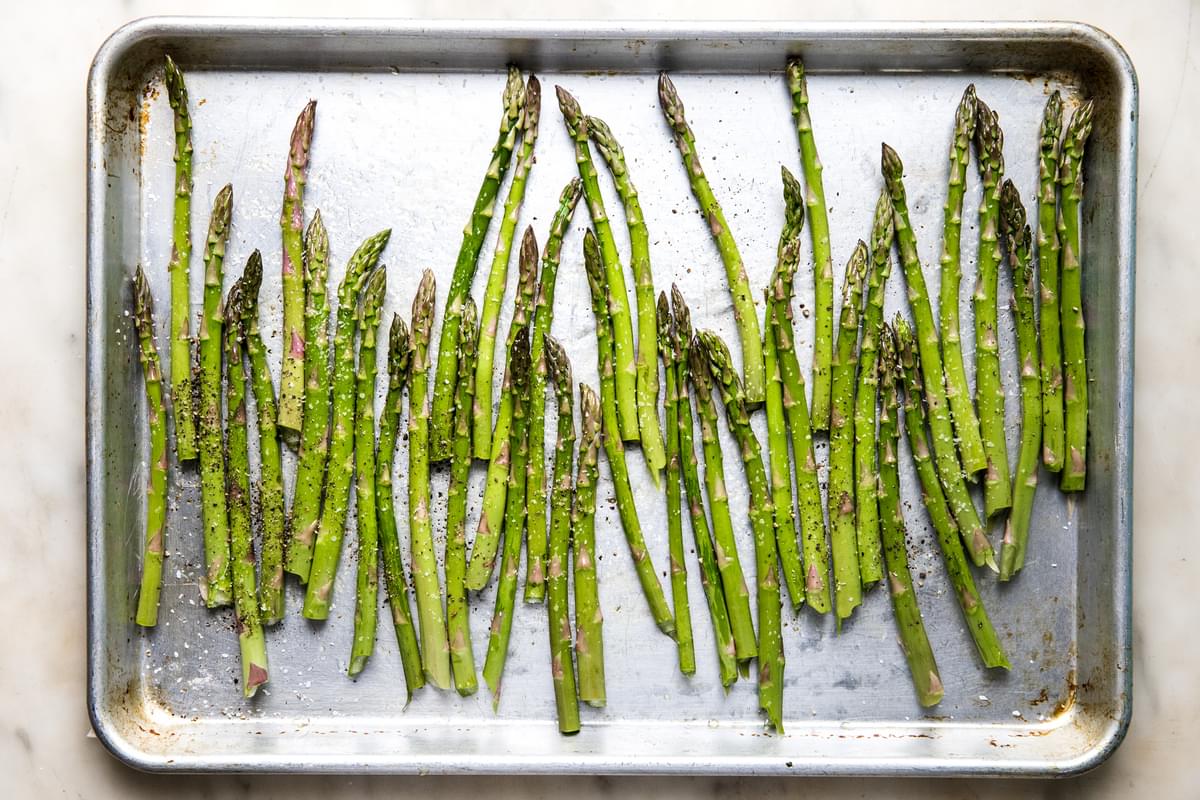 raw asparagus tossed in olive oil, salt and pepper on a baking sheet