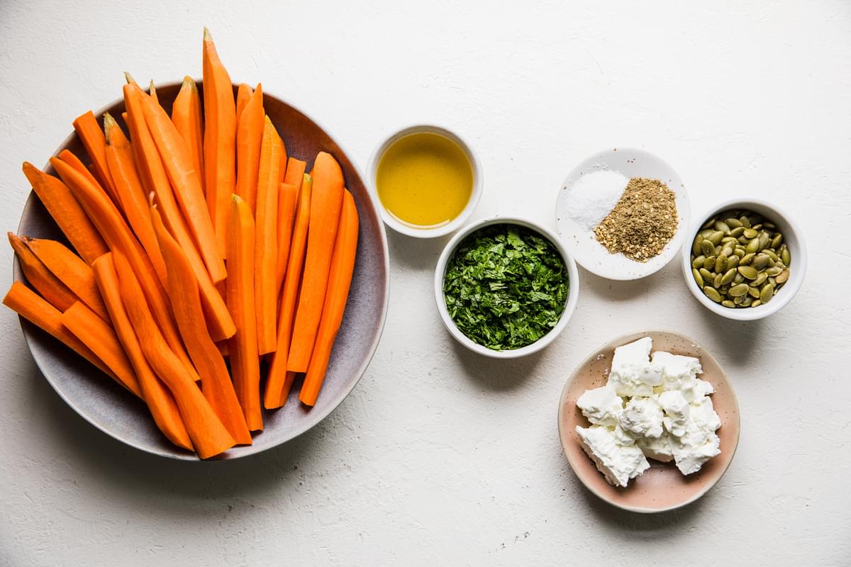 raw carrots, olive oil, cilantro, salt,, za'atar, pumpkin seeds and feta cheese in bowls on the counter
