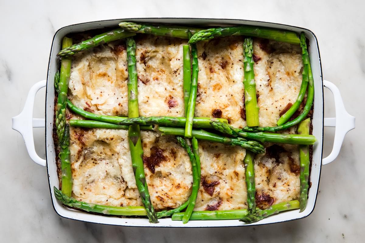 baked potato rösti mixture in a baking dish with asparagus surrounding the wells made by the back of a spoon