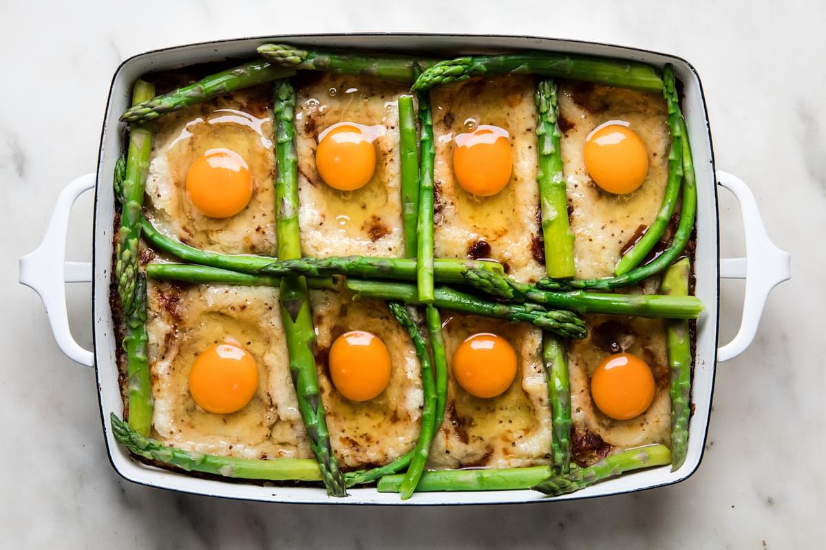 baked potato rösti mixture in a baking dish with asparagus and eggs on top