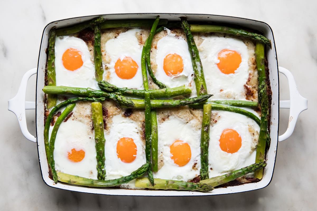 baked potato rösti mixture in a baking dish with asparagus and baked eggs on top