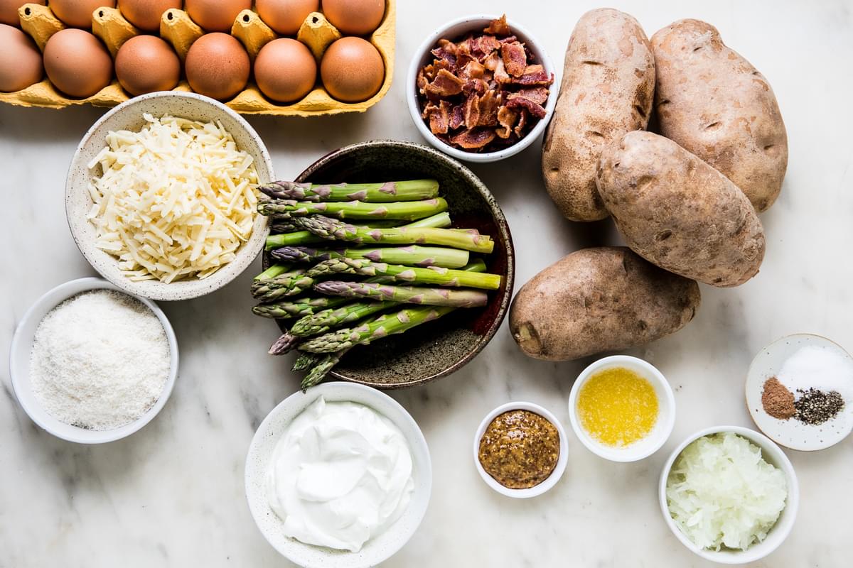 ingredients for potato rösti with eggs, shredded cheese, olive oil, sour cream and asparagus in bowls on the counter