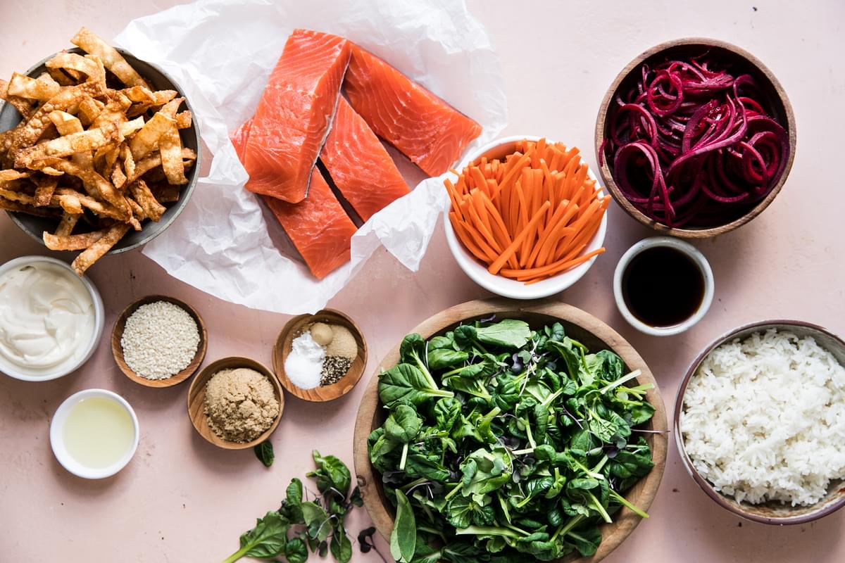 Ingredients for a rice salmon bowl, greens, rice, beets, carrots, wontons, sesame seeds, mayonnaise, ponzu and ginger
