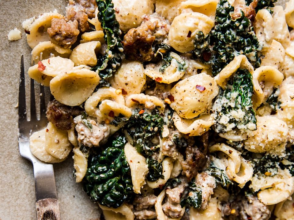 Pasta with sausage and lemon cream sauce, parmesan and kale in a bowl with a fork