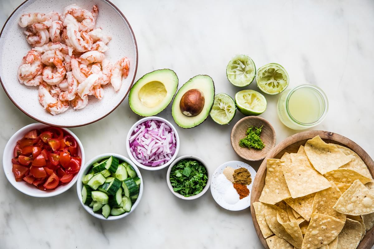 cooked shrimp in a bowl with avocado, red onion, tomatoes, cucumber, lime juice, cilantro, avocado and tortilla chips