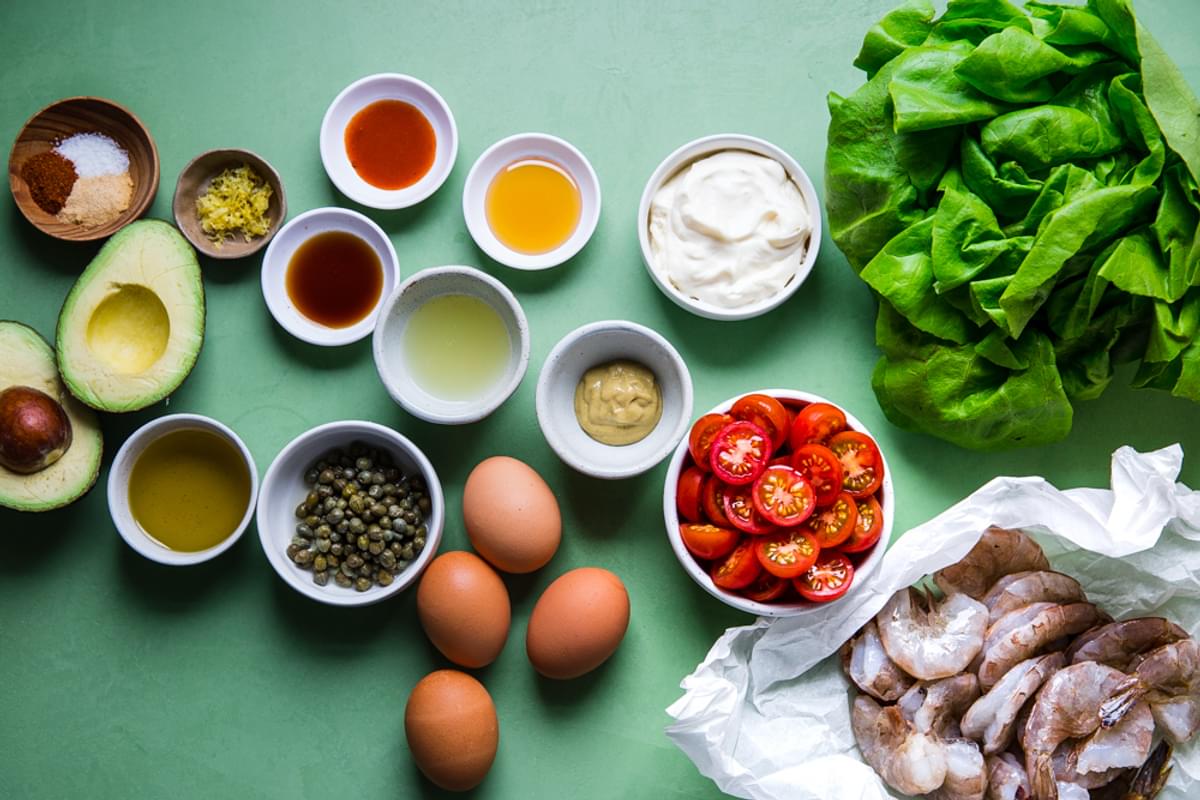 ingredients laid out for shrimp louie salad. romaine, tomatoes, hard boiled eggs, capers, avocado, mayonnaise