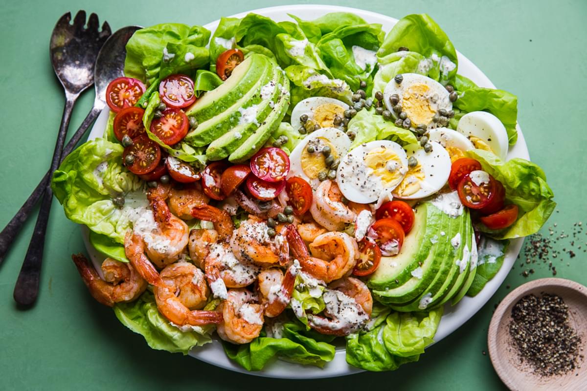 Shrimp Louie salad on a plater with avocado, romaine lettuce, hard boiled eggs, tomatoes, capers and a spicy dressing