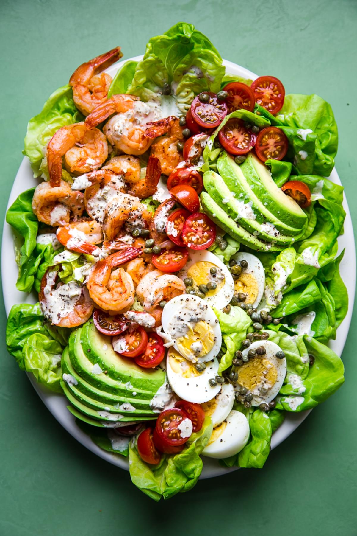 homemade Shrimp Louie salad on a plater with avocado, romaine lettuce, hard boiled eggs, tomatoes, capers and a dressing