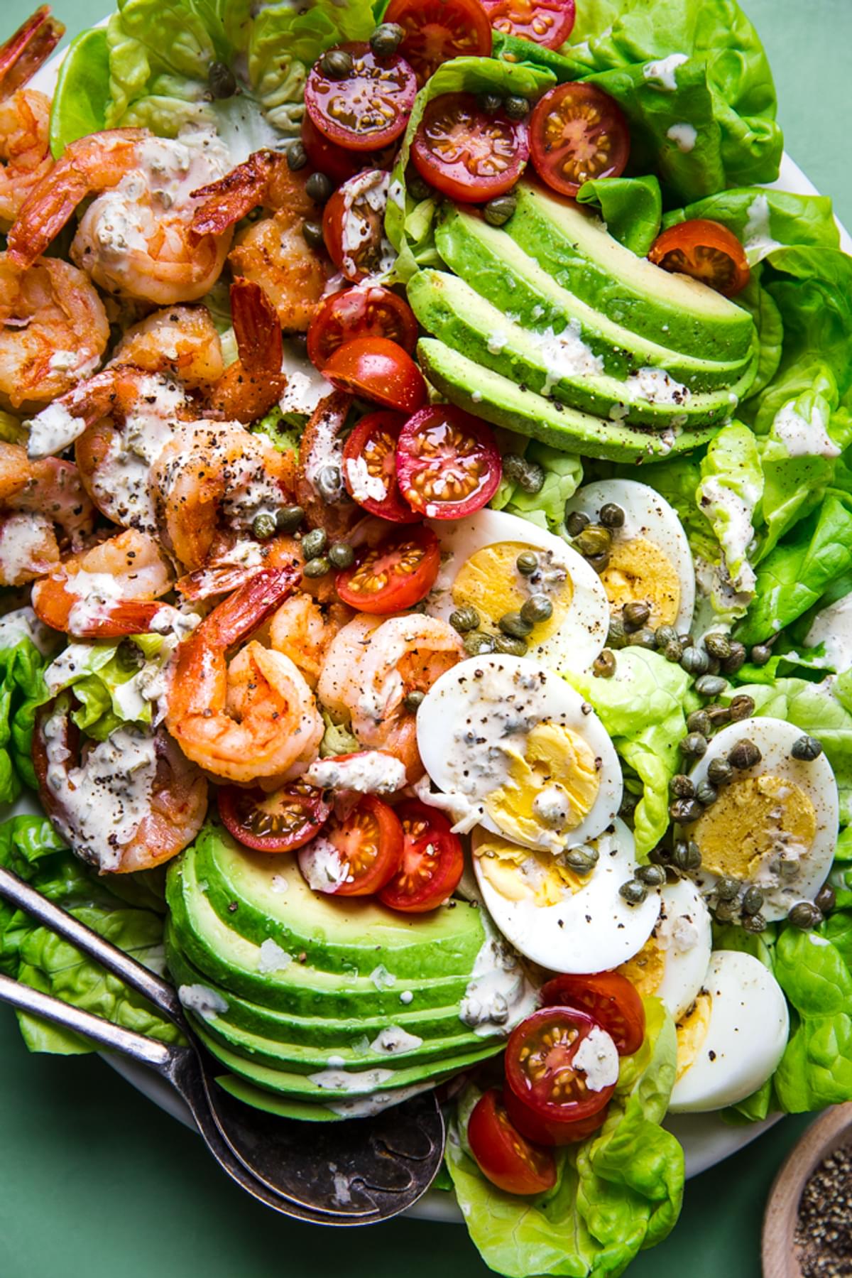 Shrimp Louie salad on a plater with avocado, romaine lettuce, hard boiled eggs, tomatoes, capers