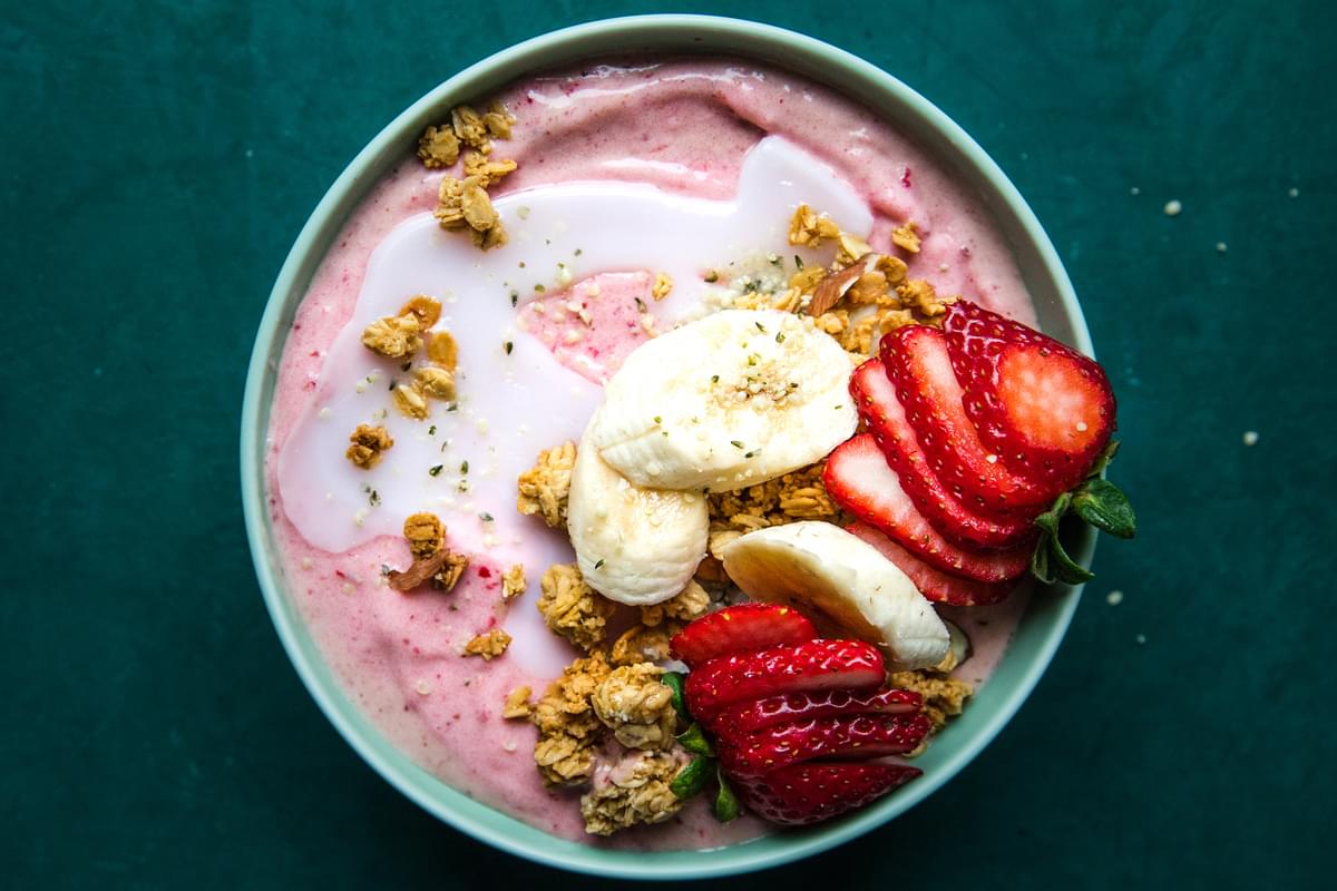 Homemade smoothie bowl topped with strawberries, bananas, granola and coconut oil