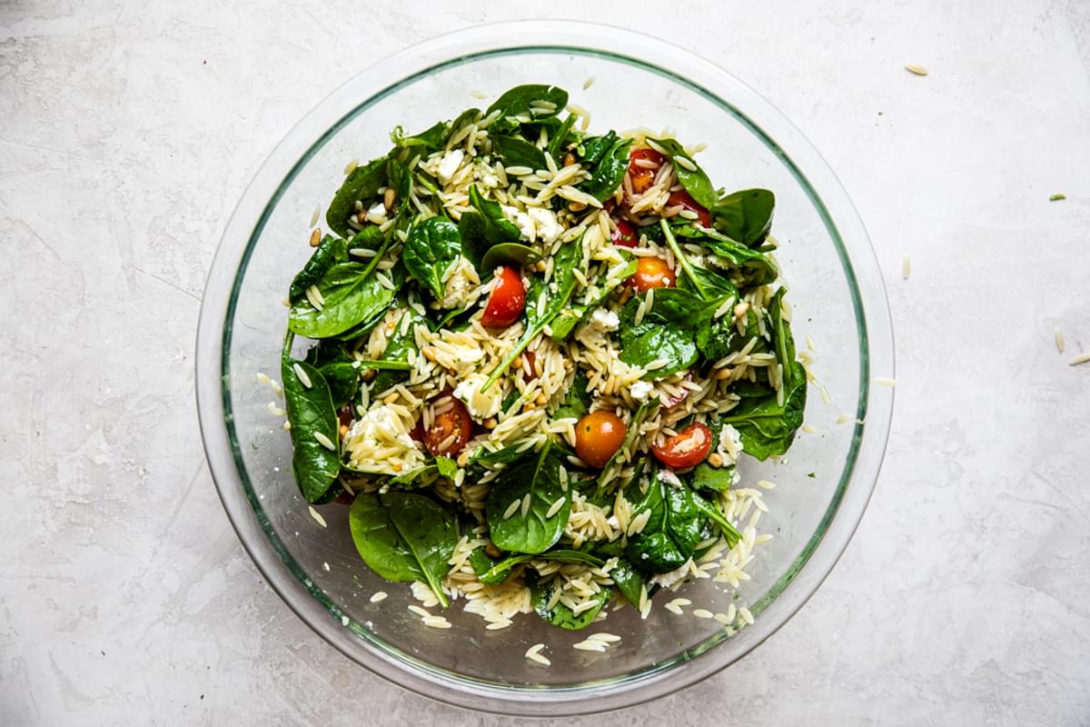 baby spinach, cherry tomatoes, feta, orzo, pine nuts and basil mixed together in a bowl