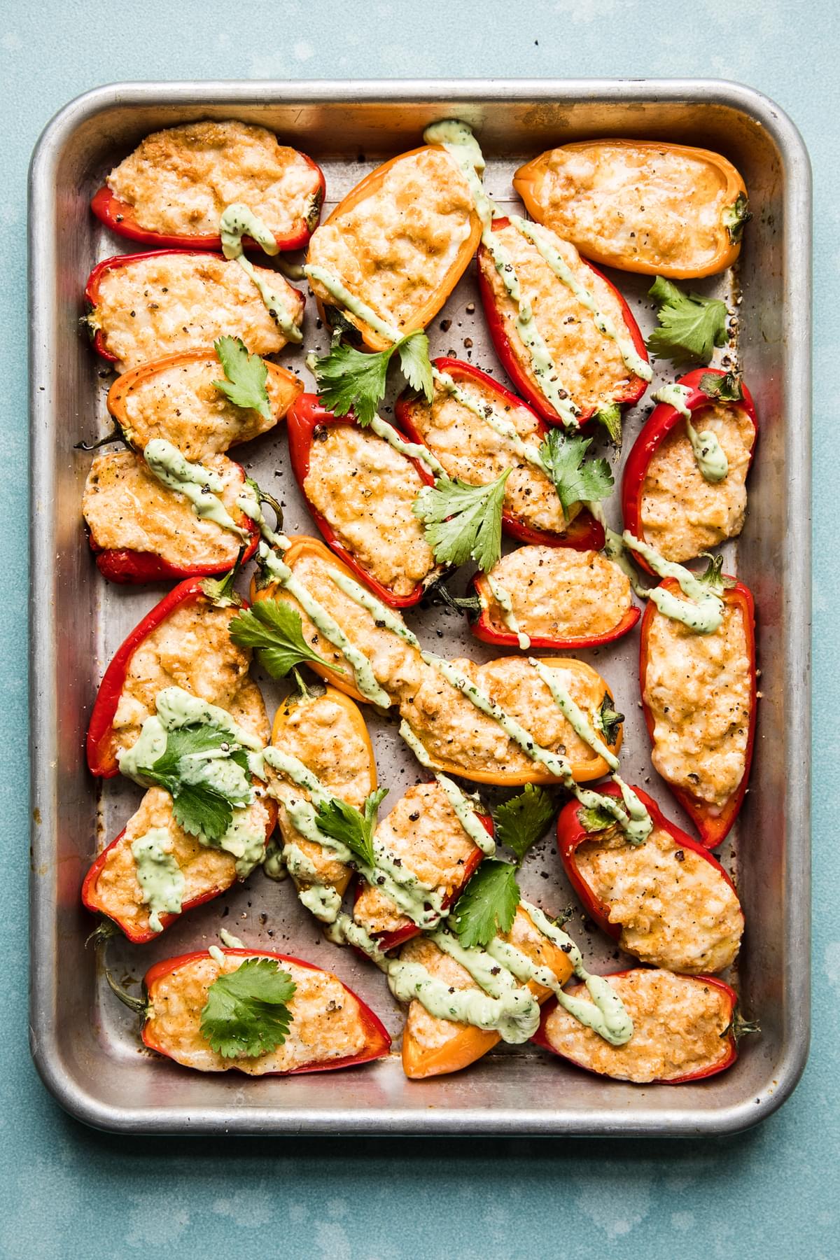 Stuffed Mini bell Peppers on a baking sheet with avocado cream and cilantro