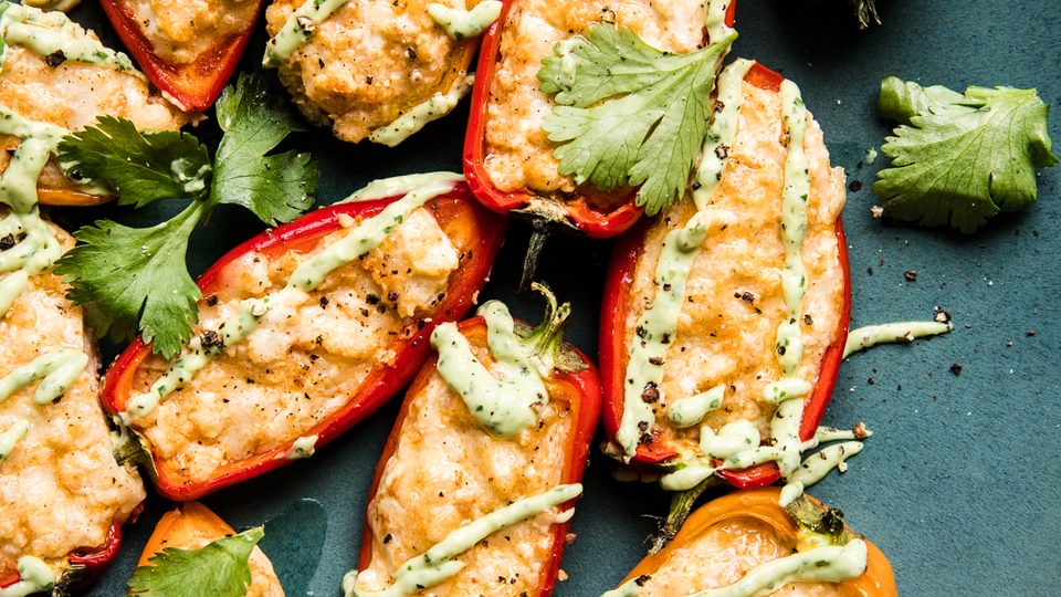 mini bell peppers stuffed with cheese and cream cheese baked in the oven with an avocado pipping sauce and cilantro