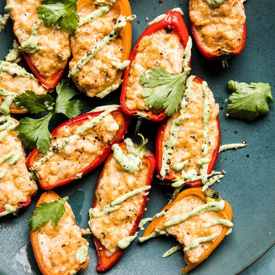 mini bell peppers stuffed with cheese and cream cheese baked in the oven with an avocado pipping sauce and cilantro