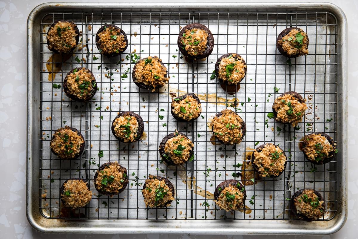 baked homemade stuffed mushrooms topped with fresh parsley on a wire cooking rack inside a baking sheet