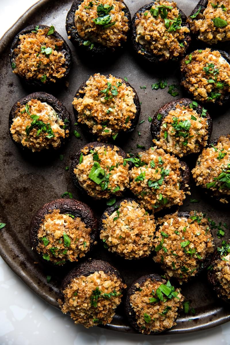 Stuffed Mushrooms made with cream cheese, Parmesan and spices topped with toasted breadcrumbs and parsley on a serving plate