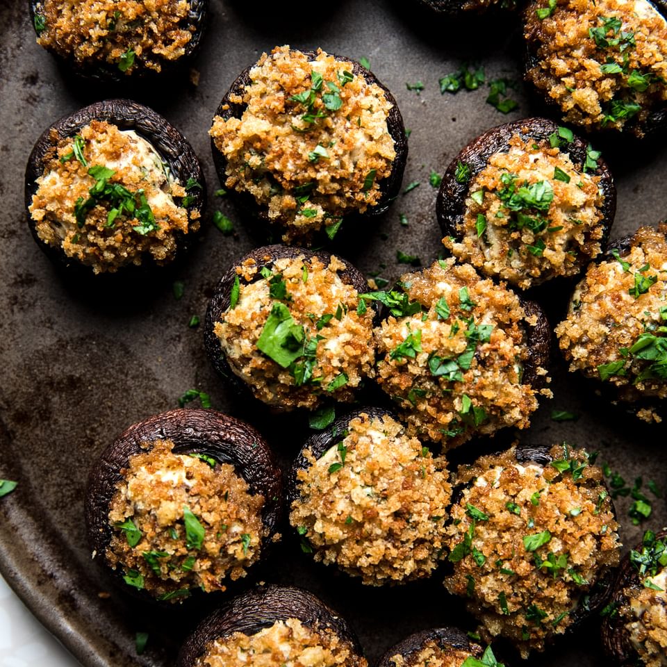 Stuffed Mushrooms made with cream cheese, Parmesan and spices topped with toasted breadcrumbs and parsley on a serving plate