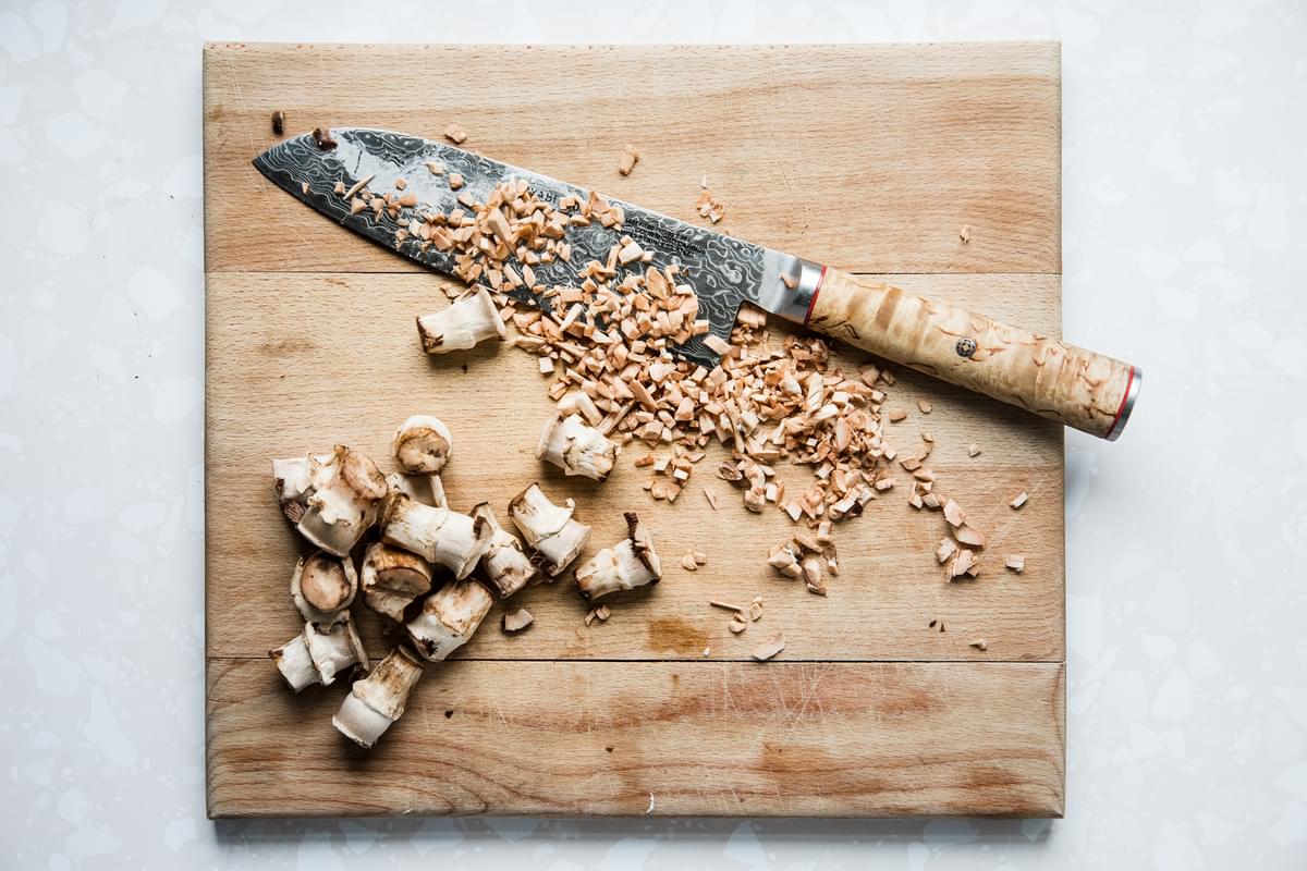 chopped mushroom stems on a cutting board with a knife