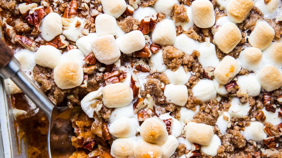 baked Homemade Sweet Potato Casserole with Marshmallows and Pecan Streusel in a baking dish being scooped with a wooden spoon