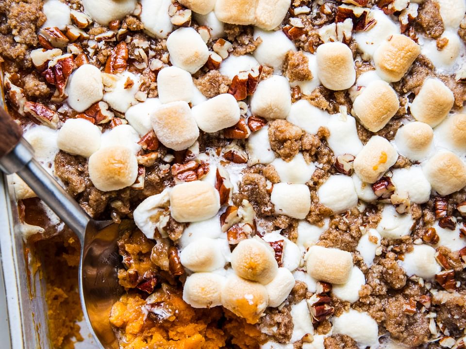 baked Homemade Sweet Potato Casserole with Marshmallows and Pecan Streusel in a baking dish being scooped with a wooden spoon