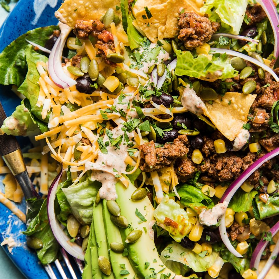 Homemade taco salad on a plate with ground beef, avocado and tortilla chips