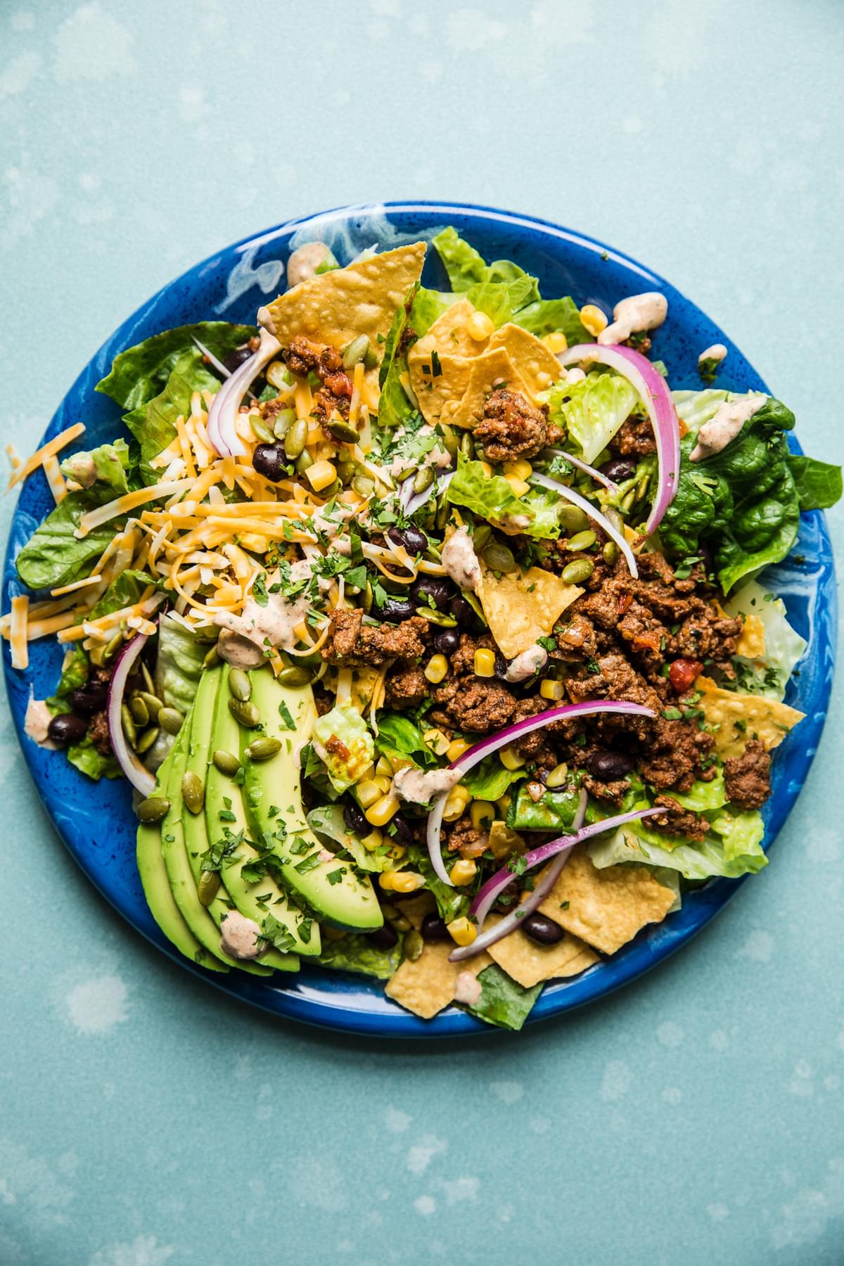 homemade taco salad recipe with corn, beans, tortilla chips, avocado and sour cream, cheese and ground taco meat