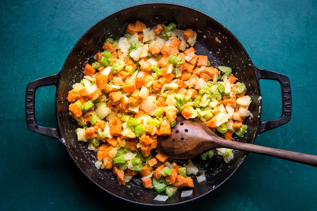 onion, celery, carrots, butter, spices and flour being stirred in a skillet with a wooden spoon