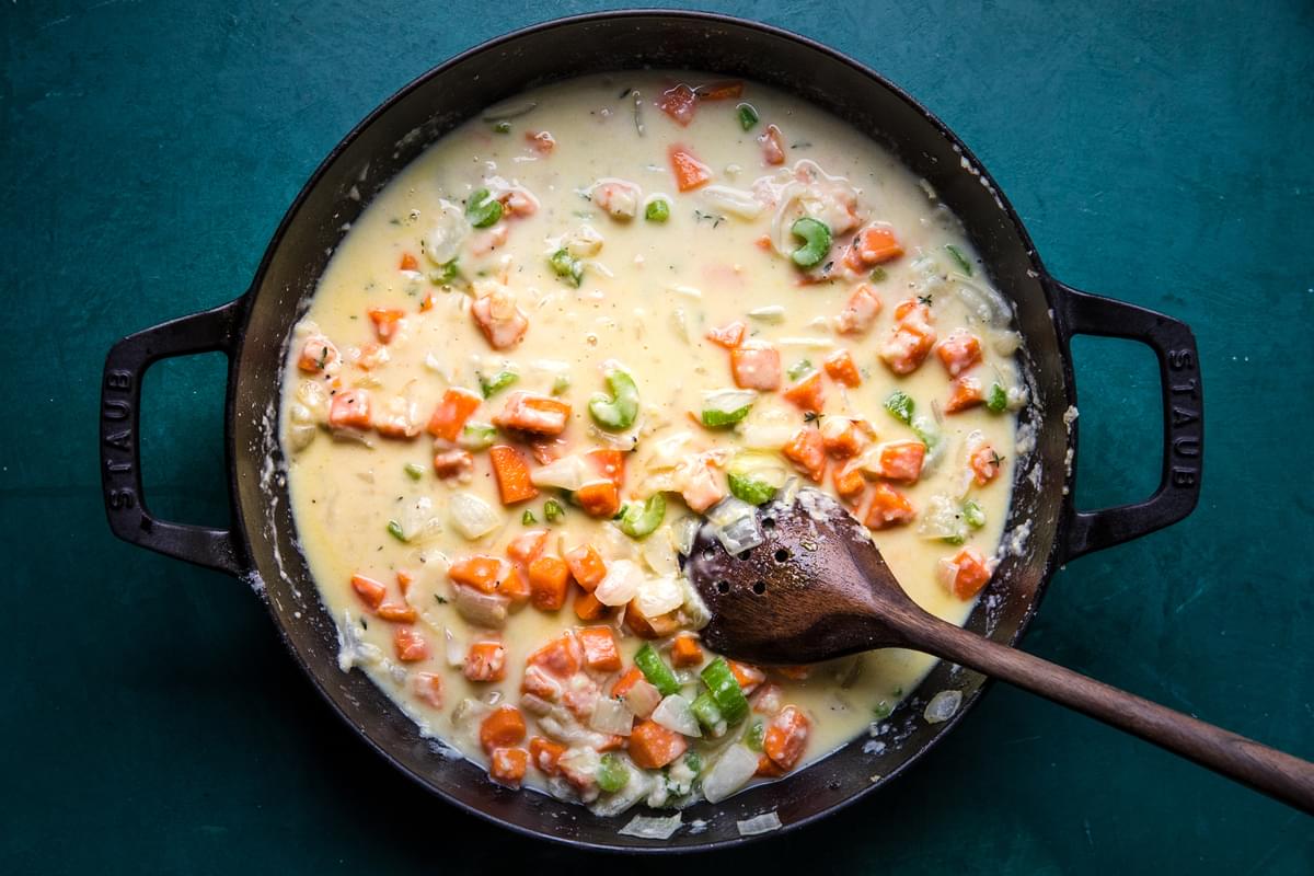 onion, celery, carrots, butter, spices, flour and milk being stirred in a skillet with a wooden spoon