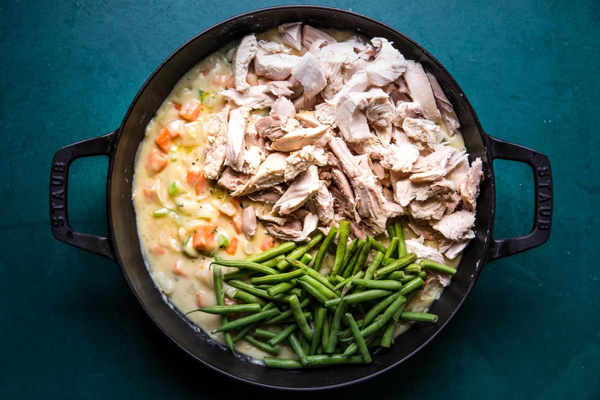 cooked onion, celery, carrots, butter, spices, flour and milk topped with green beans and  cooked turkey in a skillet
