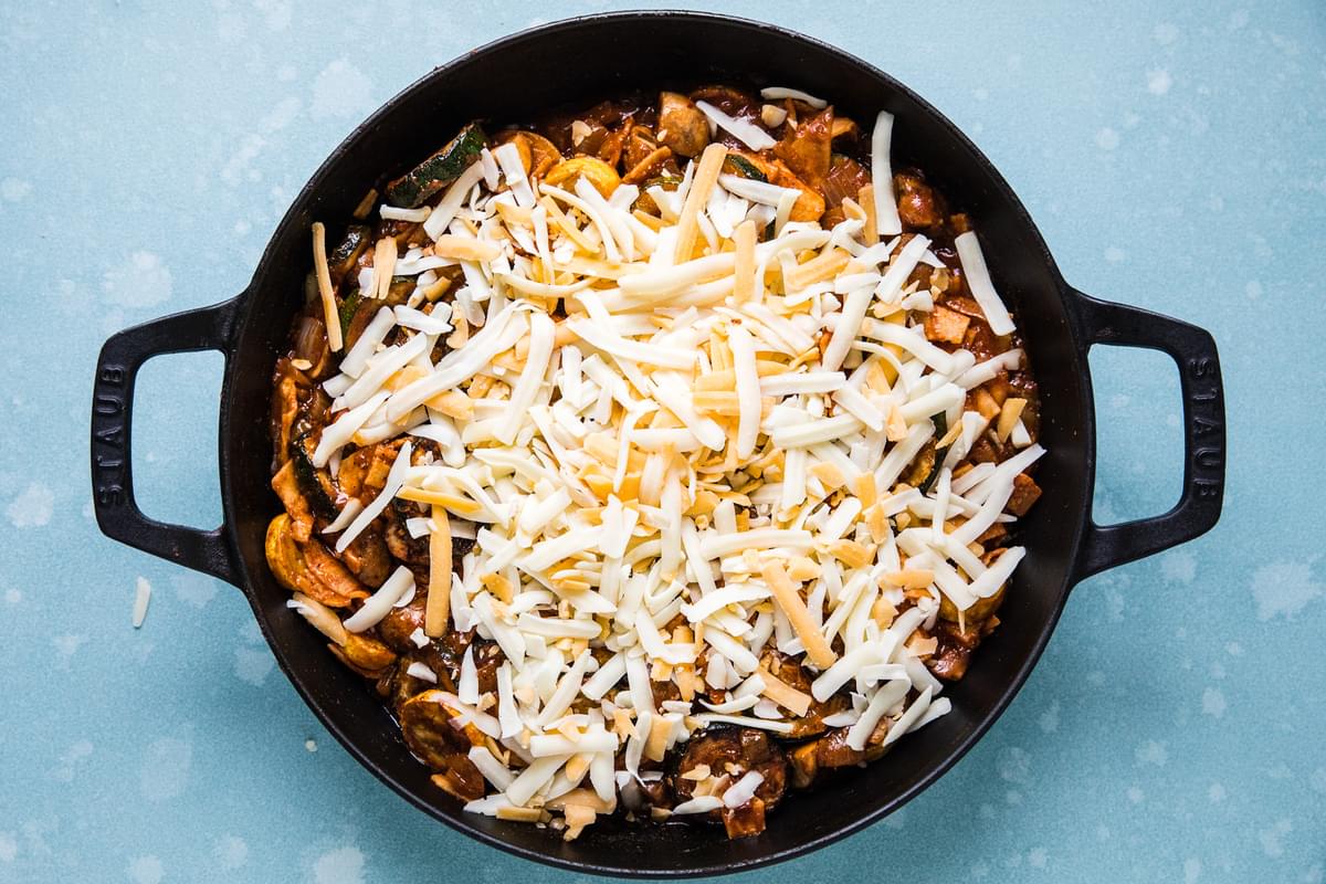 homemade vegetarian enchilada skillet topped with shredded cheese ready to be baked in the oven