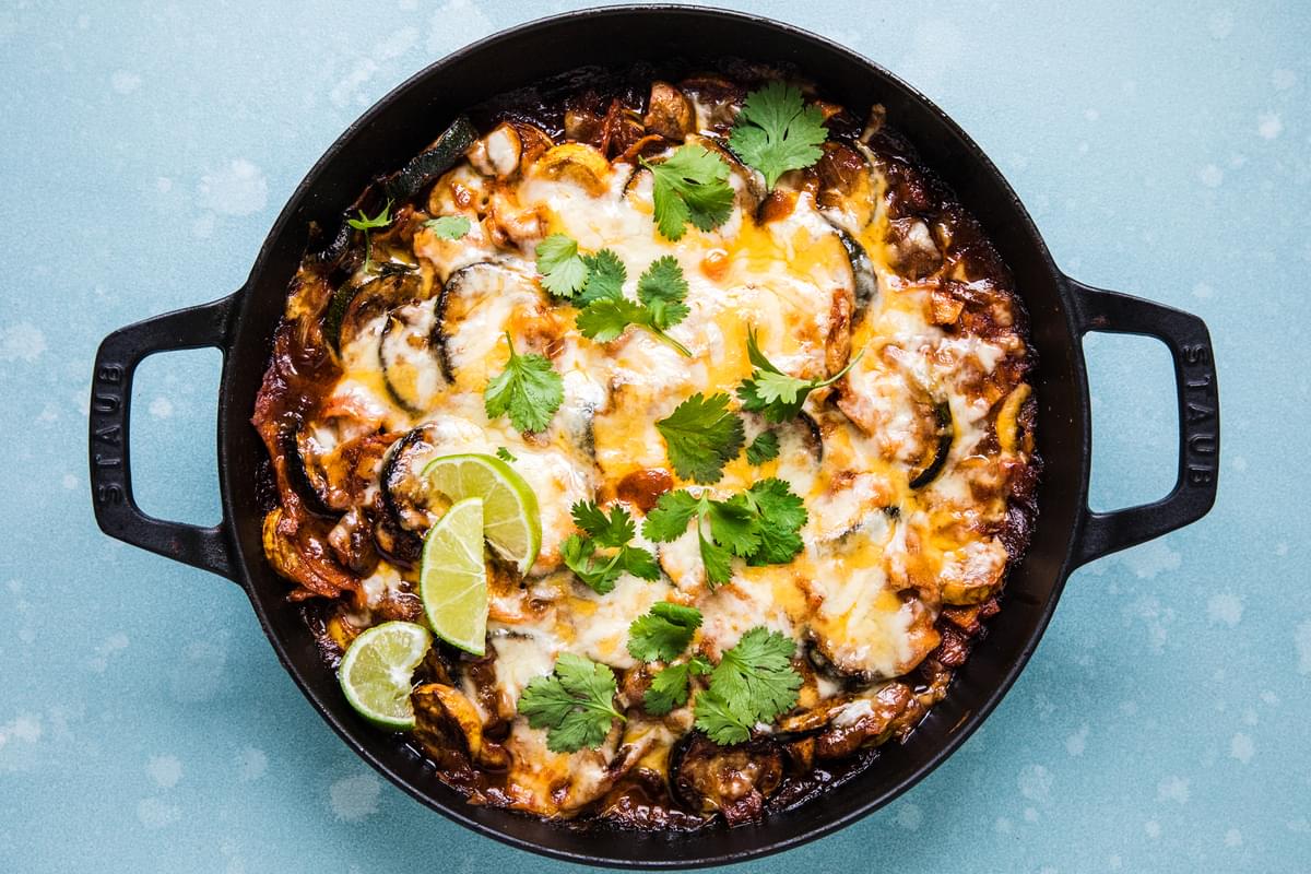 homemade vegetarian enchilada skillet topped with melted cheese, cilantro and lime wedges in a skillet on the counter