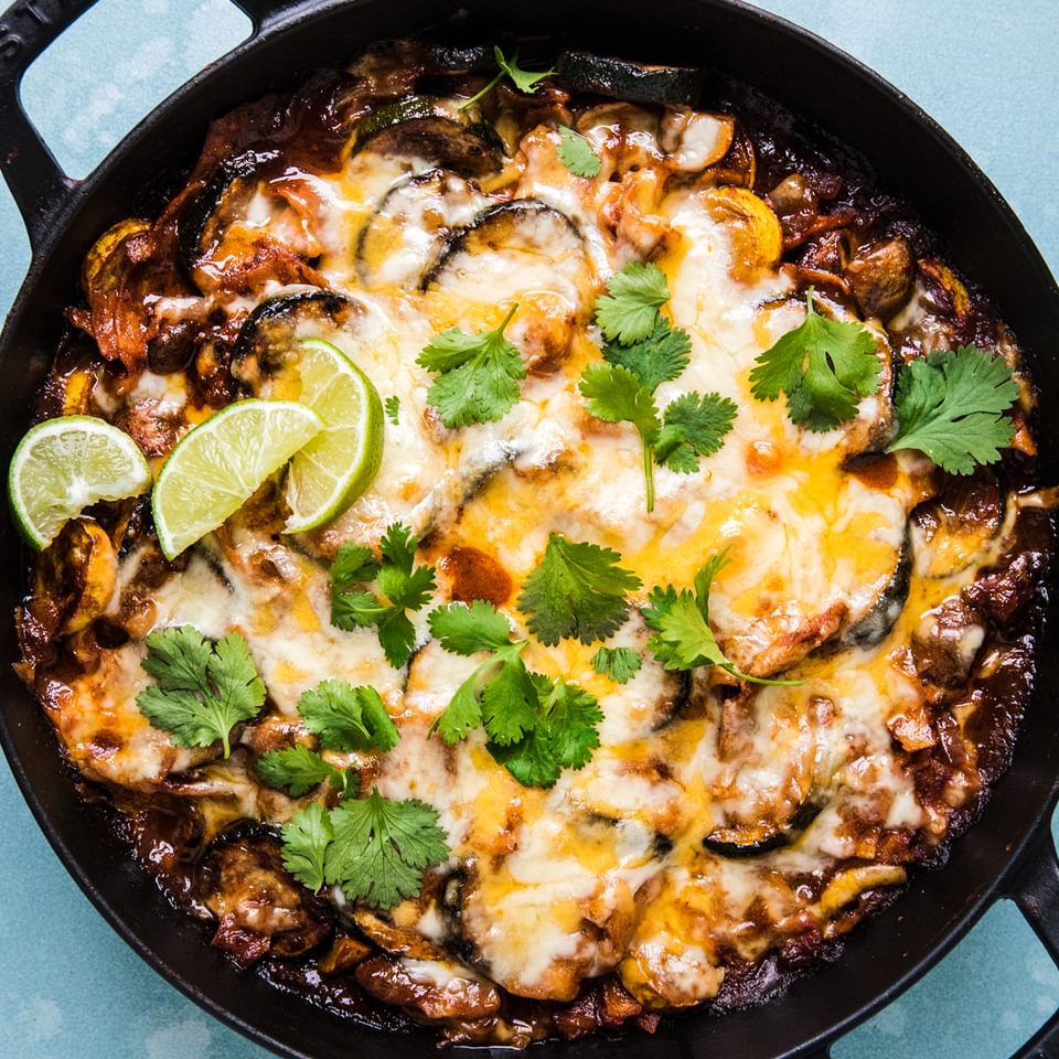 Homemade vegetarian enchilada skillet topped with cheese, cilantro and lime wedges in a skillet on the counter