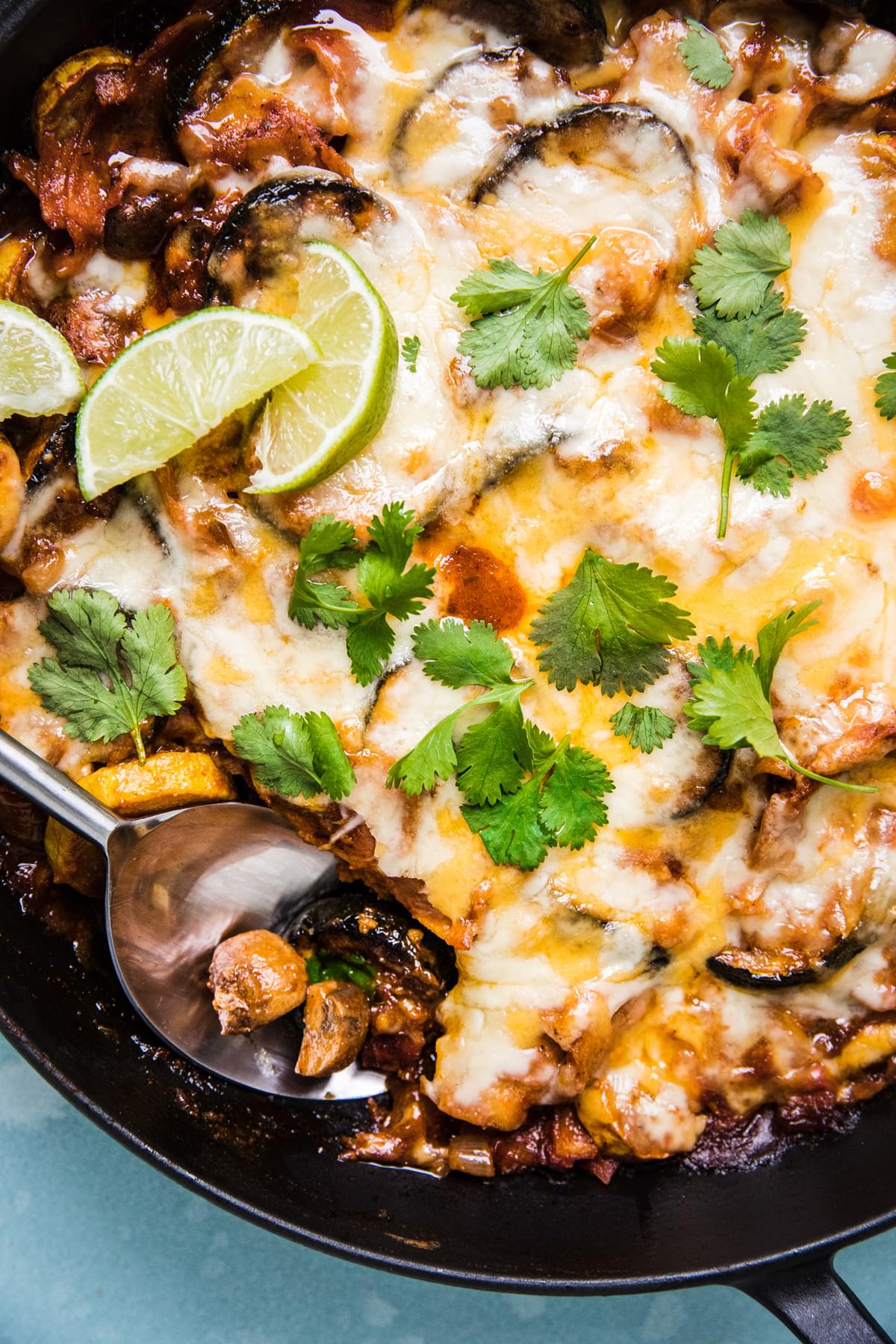 Homemade vegetarian enchilada skillet topped with melted cheese, cilantro and lime wedges in a skillet on the counter
