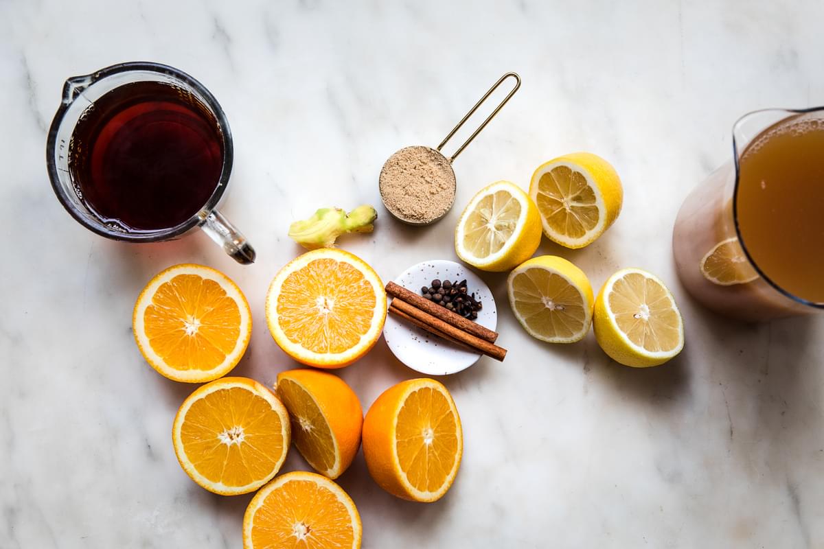 apple cider, black tea, sliced oranges and lemons, and spices on the counter
