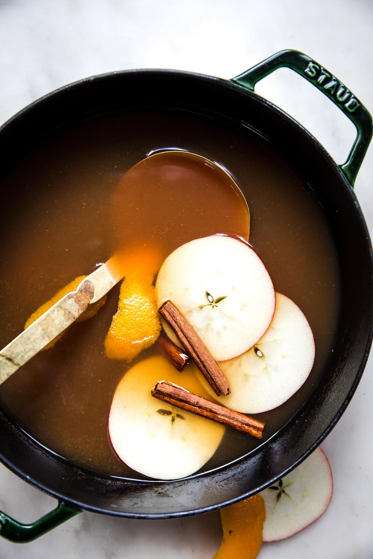 homemade wassail in a pot  with a ladle and slices apples and cinnamon sticks