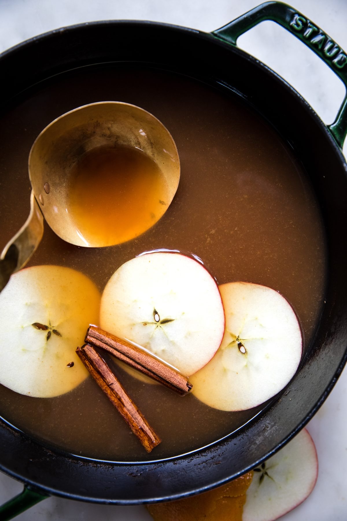 homemade wassail in a pot with a ladle and slices apples and cinnamon sticks