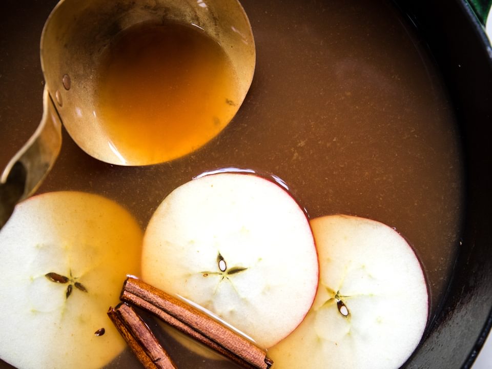 homemade wassail in a pot with a ladle and slices apples and cinnamon sticks