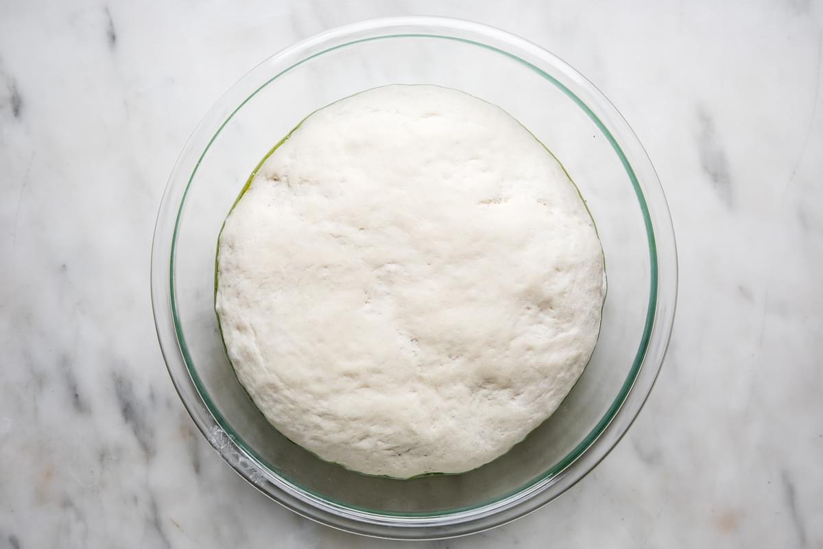 homemade focaccia bread dough rising in a bowl with olive oil