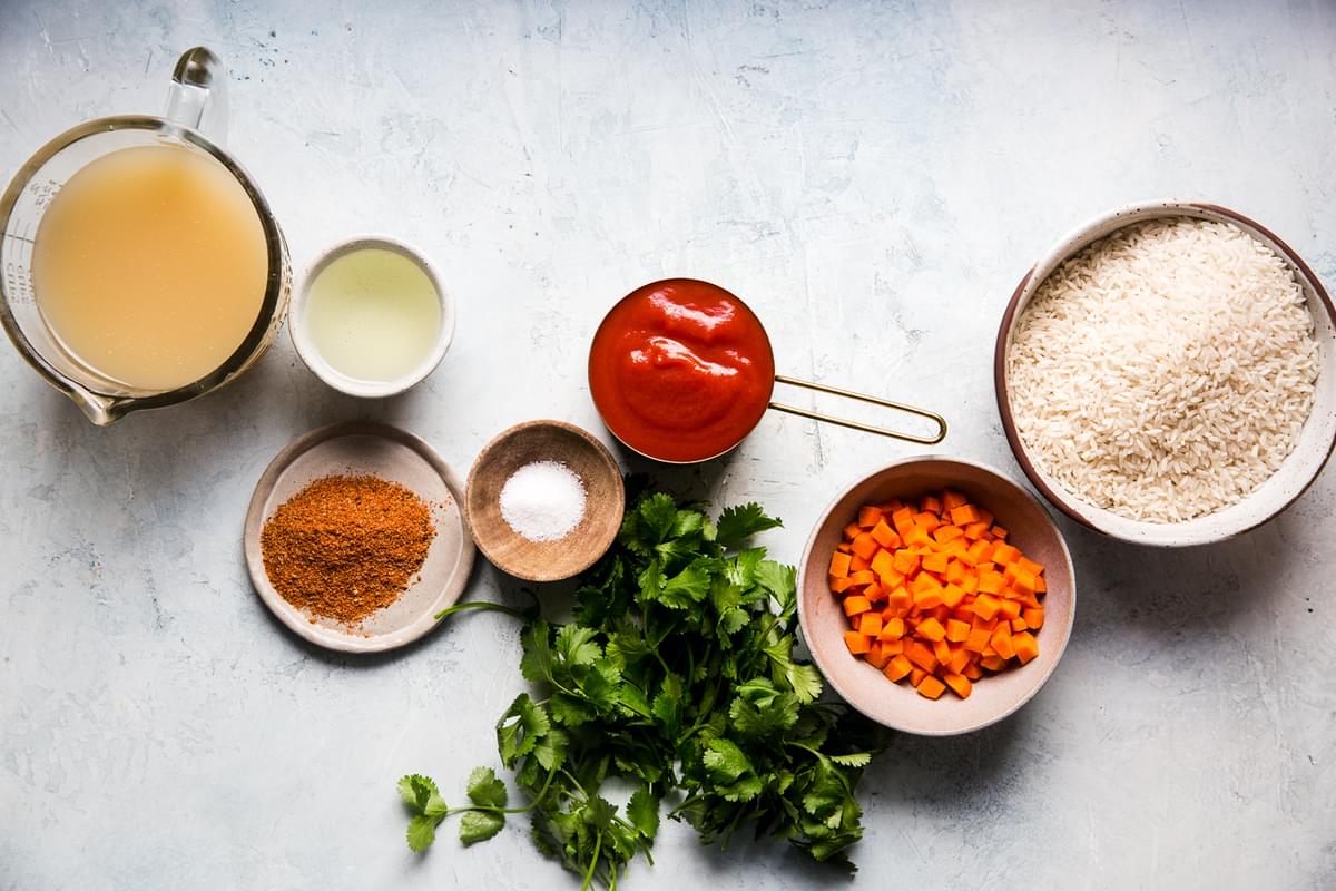 Ingredients for restaurant style Mexican rice shown in small bowls including rice, carrots, tomato sauce and taco seasoning