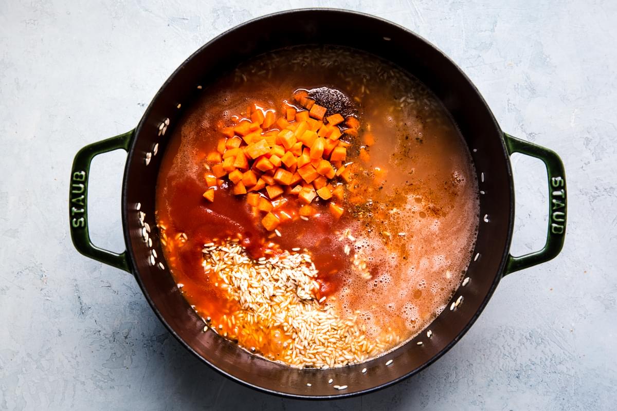 toasted rice with stock, carrots and tomatoes shown in a large pot