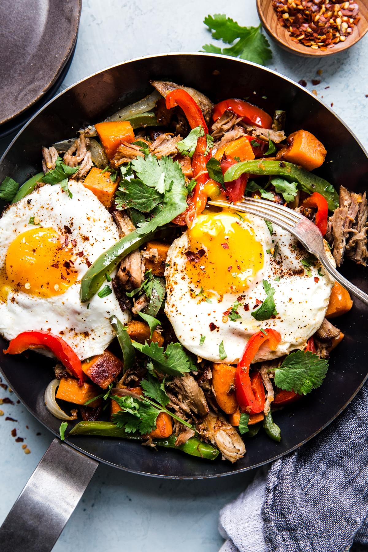 Sweet potato carnitas hash with bell peppers, fried eggs and cilantro