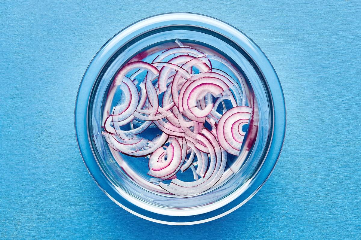 thinly sliced red onion soaking in a bowl of cold water to be used for homemade aguachile