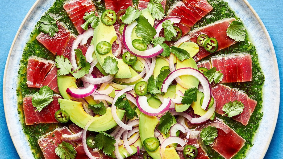 homemade aguachile on a serving platter. layered cilantro sauce, tuna, avocado slices, red onion and Serrano peppers
